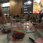 glasses of red wine at a table with prompt cards, pens and a person speaking at the front of the room with a projected image of a man tasting wine behind him - fun mindfulness activities